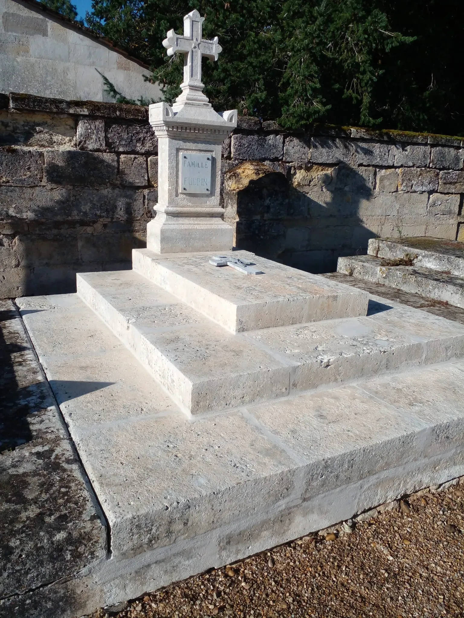 Tombe ancienne en pierre blanche surmontée d'une croix.