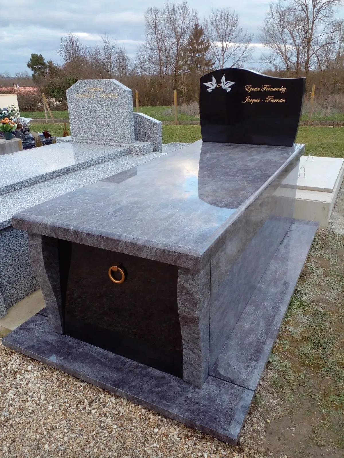 Caveau en granit gris veiné avec stèle noire et colombes.