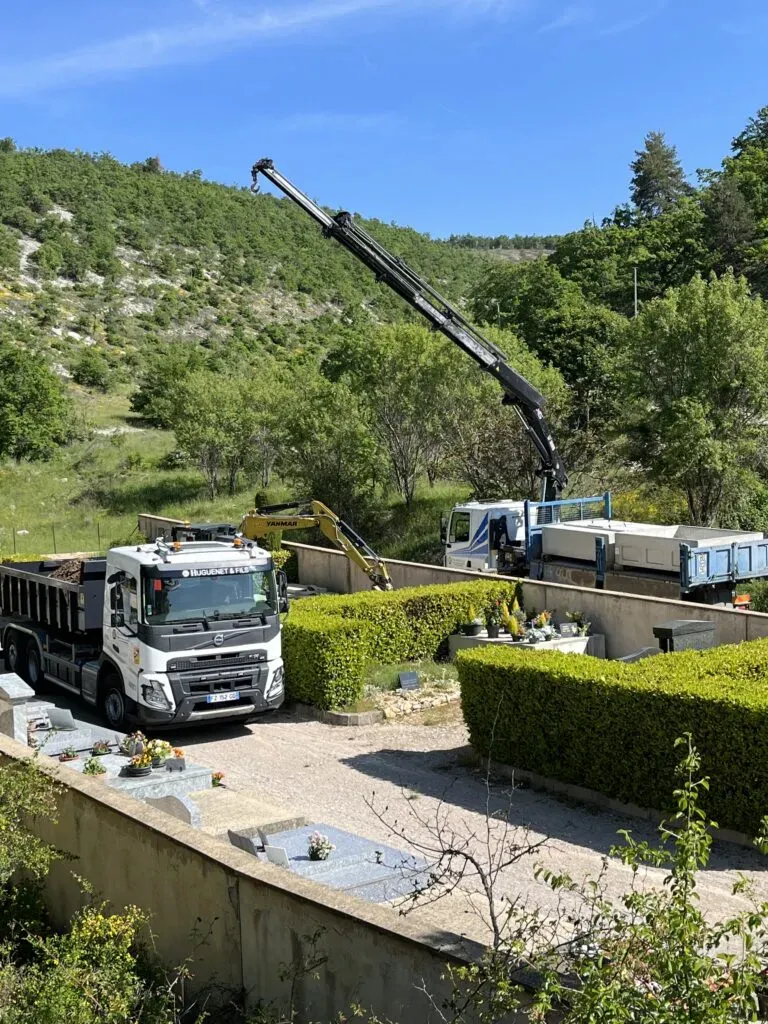 Camions de chantier et grue effectuant des travaux dans un cimetière.