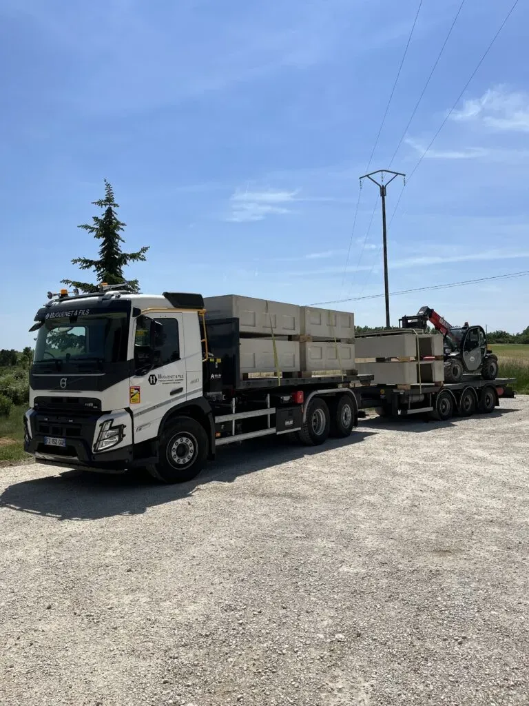 Camion semi-remorque chargé de caveaux en béton préfabriqués.