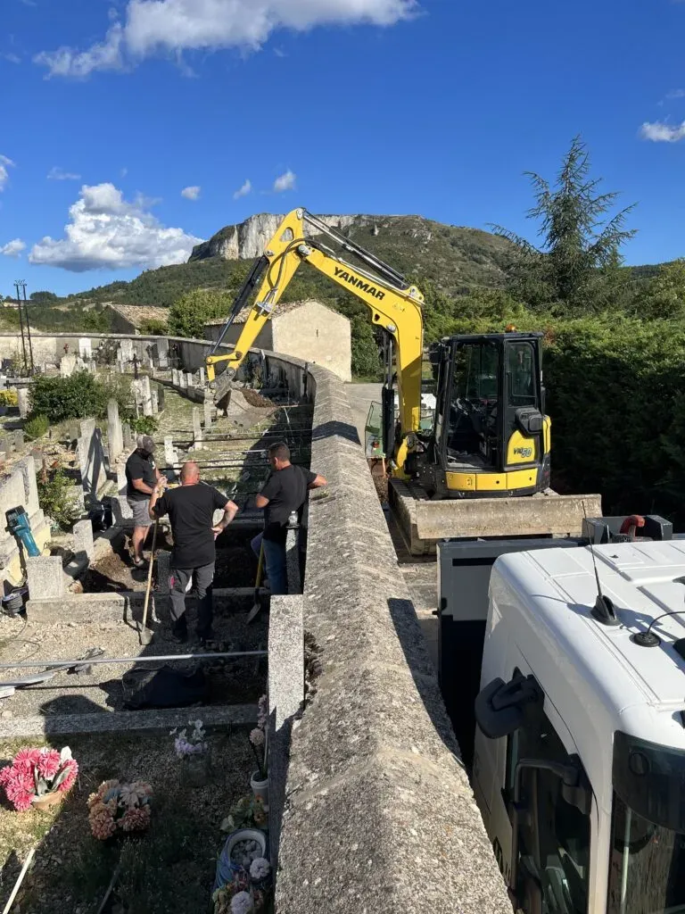 Ouvriers et mini-pelle en chantier dans un cimetière.