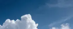 Bannière montrant un ciel bleu dégagé avec de grands nuages blancs cumulus au premier plan.