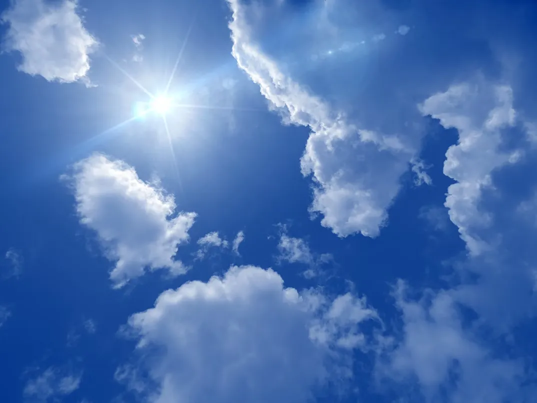 Vue en contre-plongée d'un ciel bleu ensoleillé avec quelques nuages blancs.